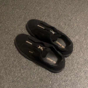 Svarta sneakers från Axel Arigato - Snygga svarta sneakers från Axel Arigato med dragkedja på ovansidan. Skorna är tillverkade i mocka och har en stilren design med låg profil. Perfekta för en modern och minimalistisk look.