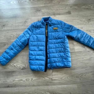 Blå pufferjacka från Barbour - Säljer en snygg blå pufferjacka från Barbour. Jackan har en dragkedja framtill och en broderad logotyp på bröstet. Perfekt för kyligare dagar med sin quiltade design och långa ärmar. Ett måste för garderoben! 💙