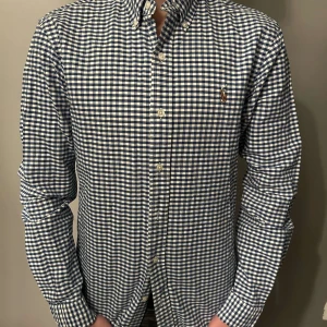 Rutig skjorta från Ralph Lauren - Snygg skjorta från Ralph Lauren i blått och vitt. Skjortan har långa ärmar och klassiska knappar framtill. Den är broderad med den ikoniska loggan på bröstet. Perfekt för en stilren look.