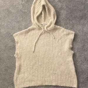 Beige stickad ärmlös hoodie från Zara - Säljer en mysig beige stickad ärmlös hoodie från Zara. Perfekt för lager-på-lager-stil med en skön huva och dragsko. Passar utmärkt för kyliga dagar när du vill ha något bekvämt och stilrent. 🧶