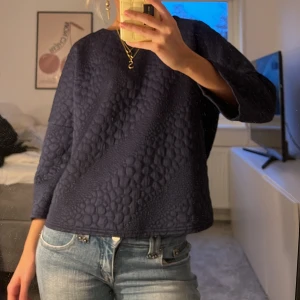 Marinblå tröja - Säljer en stilren mörkblå quiltad tröja med ett unikt mönster. Tröjan har trekvartsärmar och en avslappnad passform. Perfekt för en trendig look.