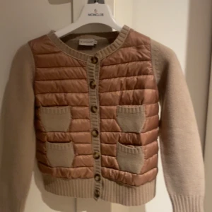 Moncler cardigan  - Säljer en snygg rosa och beige cardigan från moncler, fint skick bara en pytte liten fläck som kan gå bort har inte försökt! Har äkthetsbevis osv fråga efter fler bilder❤️