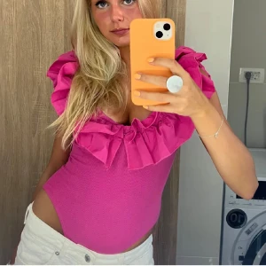 Rosa volangtopp - Snygg rosa topp med volangdetaljer runt halsen och axlarna. Perfekt för en somrig look. Toppen är tight och har en djup urringning som ger en feminin touch. RESERVERAD!! Till den 16/17:e Januari 