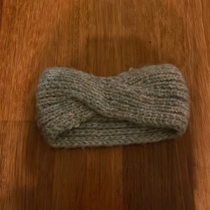 Grå stickad pannband - Säljer ett mysigt grått stickat pannband med en tvist framtill. Perfekt för att hålla värmen under kyliga dagar. Passar de flesta huvudstorlekar. Från Cubus, använd några gånger.