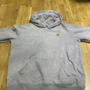 Lyle%scott hodie - Säljer en stilren grå hoodie med en liten gul logotyp på bröstet. Tröjan har en klassisk känguruficka och en bekväm huva med dragsko. Perfekt för en avslappnad stil.
