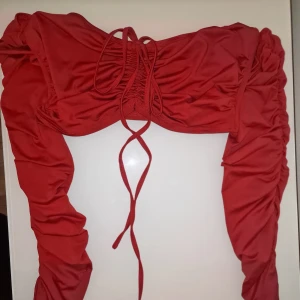 Röd crop top med snörning - Trendig röd crop top med snörning framtill och rynkade detaljer längs ärmarna. Garderobsrensning så kika gärna på övriga auktioner.