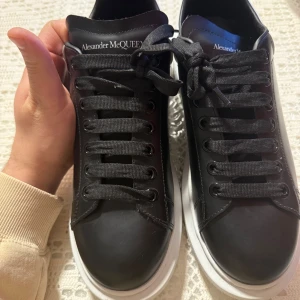 Svarta sneakers från Alexander McQueen - Snygga svarta sneakers från Alexander McQueen med vit sula och klassisk snörning. Skorna har en stilren design med märkets logotyp på baksidan och tungan. Perfekta för en trendig look.