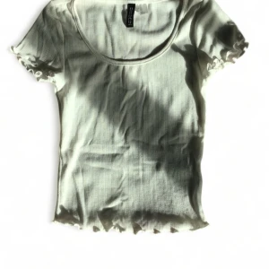 Vit ribbad topp från Divided - Säljer en söt vit ribbad topp från Divided. Den har korta ärmar med volangdetaljer och en rund halsringning.