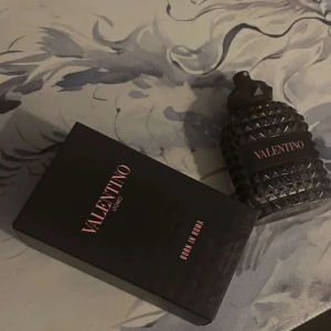 Valentino Uomo Born in Roma -  De är ungefär 20 ml kvar av 50 ml, jag tar emot byten också !   Säljer en lyxig parfymflaska från Valentino, Uomo Born in Roma. Flaskan har en elegant design med ett mönster av små pyramidformade nitar och en mörk färgton. Perfekt för den som vill ha en sofistikerad doftupplevelse.  