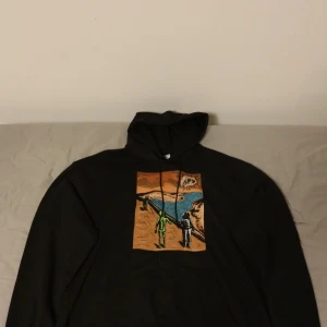 Hoodie med designertryck - Säljer en svart hoodie med ett grafiskt tryck på framsidan. Hoodien har en dragsko i huvan. Strl XL oversize