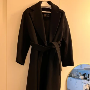 Svart kappa från Zara - Elegant svart kappa från Zara med knappar och bälte i midjan. Tillverkad av premiumtyg från Manteco. Perfekt för kyligare dagar med sin stilrena design och långa ärmar. Den är i gott skick men lite dammig men det är enkelt att rolla bort. Köpt för 2 år sedan och nypris ca  2 000kr. 