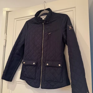 Mörkblå quiltad jacka från Bondelid - Snygg mörkblå quiltad jacka från Bondelid med dragkedja och knappar. Jackan har en bröstficka med dragkedja och två framfickor med knappar. Perfekt för höst och vår. Köpt för 1500kr