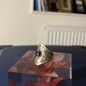 Silverring 925 med äkta röd sten - Unik silverring med en vacker röd sten i centrum. Ringen har ett flätat mönster som ger den en elegant och rustik känsla. Perfekt för att ge en touch av stil till vilken outfit som helst.