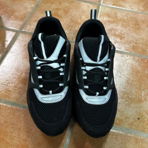 Svarta sneakers från Dior - Snygga svarta sneakers från Dior med vita detaljer och snörning. Tillverkade i Italien, dessa skor kombinerar stil och komfort med en modern design.