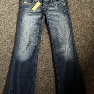 Blå jeans från Diesel - Snygga blå jeans från Diesel med broderade detaljer på bakfickorna. Modellen är 'Lambry' och har en klassisk femficksdesign med guldfärgade knappar. Prislappen är kvar, nytt skick. Priset går att diskutera:)