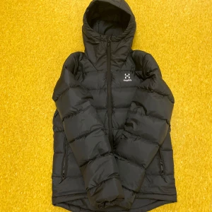 Svart Haglöfs puffer jacka - Säljer en svart puffer jacka från Haglöfs med huva och dragkedja. Jackan är perfekt för kalla dagar och har en stilren design med två sidofickor med dragkedjor. Jackan är använd max 2-3 gånger  Säljer jackan för 1799kr Köpt sedan höst start för 2299 på rea! Jackan kostar 3199kr på orginal pris!! 