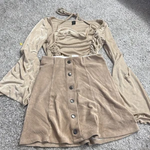 Beige glittrig topp med vida ärmar - Snygg beige topp med glittrigt tyg och vida ärmar. Toppen har en knytning i nacken och rynkade detaljer framtill. Perfekt för en festlig look! Två delar för 100kr