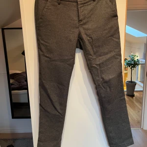 Grå flanellbyxor från Mason’s - Snygga grå kostymbyxor från Mason’s i en klassisk design. Byxorna har en rak passform med knappar bak och diskreta fickor fram. Perfekta för en stilren look. Litet i hål i skrevet som är lätt och laga och inte syns