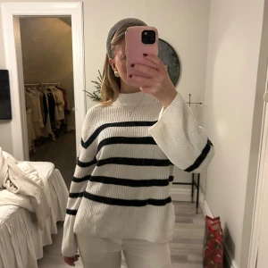 Vit randig stickad tröja - Säljer en snygg vit stickad tröja med svarta ränder. Tröjan har långa ärmar och en bekväm passform. Perfekt för en stilren look.