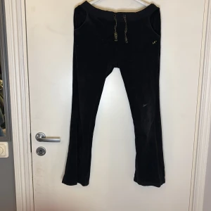 Svarta lågmidjade mjukisbyxor med snörning - Säljer ett par svarta lågmidjade mjukisbyxor med snörning i midjan och broderad detalj. Byxorna har bootcut passform och är perfekta för en avslappnad stil.