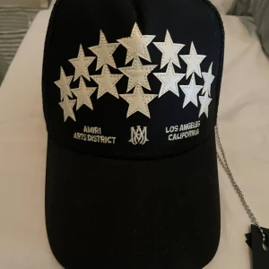 Svart keps med stjärnor från Amiri - Snygg svart keps från Amiri med silverfärgade stjärnor och texten 'Arts District Los Angeles California'. Perfekt för en cool och avslappnad stil.