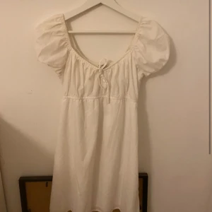 Vit klänning från Hollister - vit klänning från Hollister i bra skick med puffiga kortärmar och en söt knytning framtill. Den har en smockad överdel som ger en bekväm passform. Funkar som student klänning