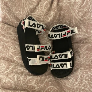 Svarta sandaler från Fila - Snygga svarta sandaler från Fila med justerbara remmar i vitt med Fila-logga i svart och rött. Perfekta för en avslappnad stil och till sommaren.