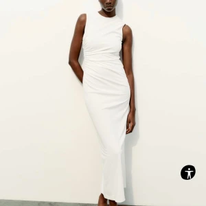 Vit  långklänning från zara - Elegant vit långklänning med ärmlös design och smickrande drapering i midjan. Klänningen har en stilren slits baktill för extra rörelsefrihet. Aldrig använt etiketten är på, Storlek XS men passar även S