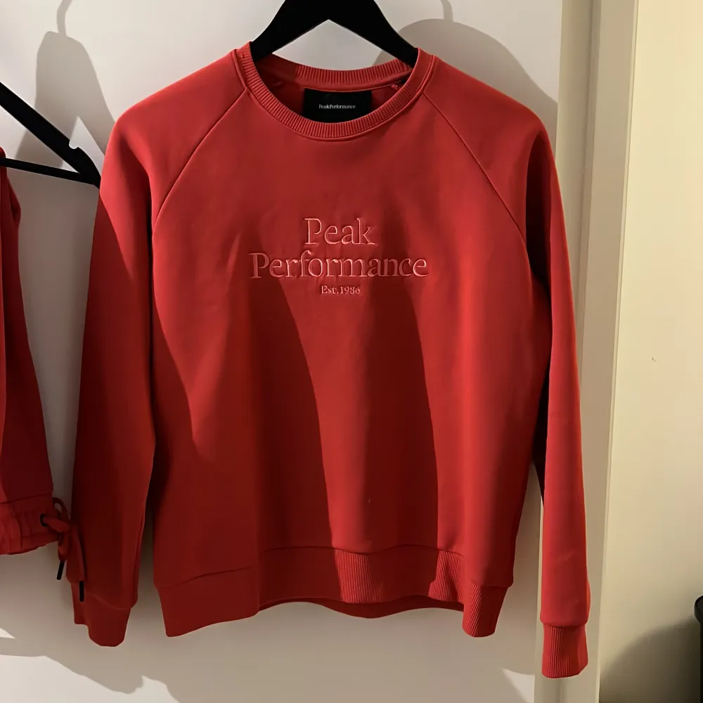 Säljer en snygg röd sweatshirt från Peak Performance med broderad logga på framsidan. Tröjan har långa ärmar och ribbade muddar vid ärmslut och nederkant. Perfekt för en avslappnad stil.. Neuletakit & Villapaidat.