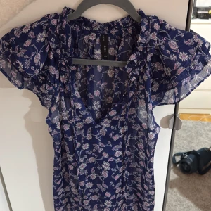 Blommig blå lila blus från mango - Söt blå lila blus med blommigt mönster från  mango. Den har en v-ringad design och korta ärmar med volangdetaljer. Perfekt för en somrig look!