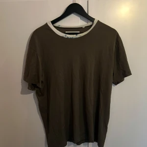 Our legacy t-shirt 2014 - Säljer en brun t-shirt från Our Legacy med en vit ribbad krage. T-shirten har en enkel och stilren design med korta ärmar. Perfekt för en avslappnad look. Finns i stockholm! 