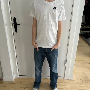 Vit barn t-shirt från Nike - Säljer en klassisk Nike T-shirt i storlek 157–168 cm med rund halsringning och deras ikoniska Nike logga på bröstet. T-shirten är kortärmad och tillverkad i bomull, perfekt för en avslappnad stil.