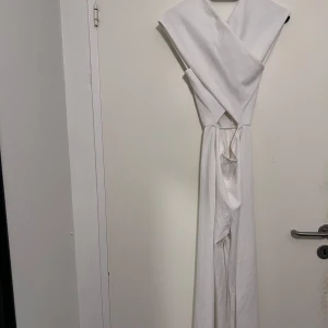 Vit  jumpsuit från NLY One - Elegant vit omlott jumpsuit från NLY One i storlek XS. Jumpsuit har en stilren design med knytband i midjan och är ärmlös. Perfekt för sommarens festligheter.
