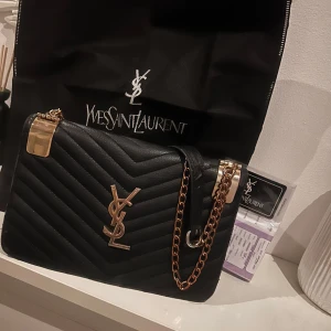 Svart axelväska från Saint Laurent - Snygg svart axelväska från Saint Laurent med quiltad design och guldfärgade detaljer. Väskan har en kedja som axelrem och det ikoniska YSL-emblemet på framsidan. 