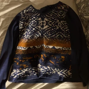 Mönstrad tröja från Signature - Säljer en snygg mönstrad tröja från Signature i mörkblått med inslag av vitt och orange. Tröjan har långa ärmar och ett unikt mönster framtill som ger en cool look. Perfekt för att liva upp garderoben!