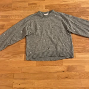 Grön stickad tröja med pärlor från H&M - Säljer en grön stickad tröja från H&M dekorerad med pärlor. Tröjan har långa ärmar och ribbade kanter vid hals, ärmslut och nederkant. Perfekt för kyligare dagar! Använd många gånger men ser nästan ny ut.