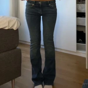 Blå bootcut jeans  - Snygga blå bootcut jeans med låg midja. Perfekta för en avslappnad stil. Klassisk femficksdesign och dragkedja med knappstängning.