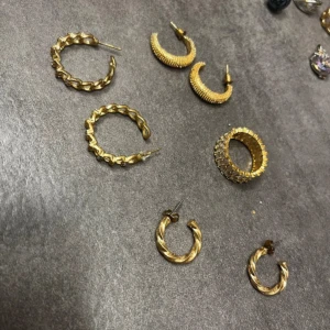 Guldiga örhängen i olika stilar - Samling av guldiga örhängen i olika stilar. Inkluderar flätade och texturerade hoops samt små, eleganta ringar. Perfekt för att mixa och matcha till olika tillfällen.