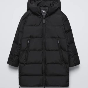 Svart dunjacka från Zara - Snygg svart dunjacka från Zara med dragkedja och huva. Perfekt för kyliga dagar med sin långa design och praktiska fickor med dragkedja. En stilren och funktionell jacka för vintern. Pris kan diskuteras