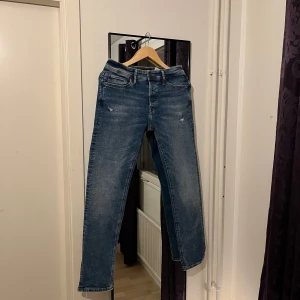 Blå jeans med slitningar - Snygga blå jeans med lätt slitna detaljer för en trendig look. De har en klassisk femficksdesign och en bekväm passform. Perfekta för en avslappnad stil.