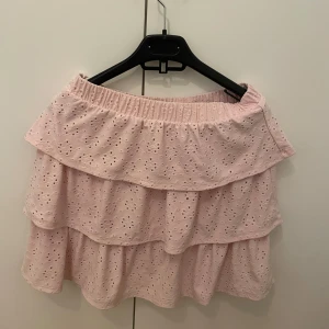 Rosa kjol från Vila - Söt rosa kjol från Vila med volangdetaljer och broderat mönster. Perfekt för en somrig look. Kjolen har en elastisk midja för bekväm passform.