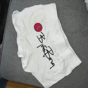 Vita mjukis shorts från Björn Borg - Säljer ett par vita Björn Borg shorts med en röd tennisboll och svart signaturtryck. De har en bred resår i midjan och strass detaljer på märket på framsidan (bild 2). På baksidan är ett stort ”Björn Borg” tryck (bild 1)  väldigt gamla men har mycket kvar att ge! Super bra skick