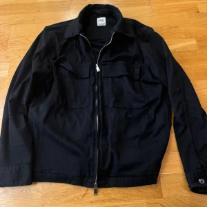 Svart jacka från Zara - Snygg svart jacka från Zara med dragkedja och krage. Jackan har två bröstfickor med lock och långa ärmar. Perfekt för en stilren look.