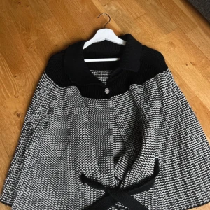 Svartvit poncho - Elegant svartvit stickad poncho (Blair Waldorf vibes!) med ett dekorativt knytband i midjan och en glittrig knappdetalj (saknar några diamanter) framtill. Lite för stor för mig, därför säljs! Skulle säga den passar S till M hållet.