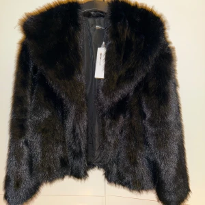 Svart pälsjacka från Gina Tricot med en lyxig känsla. - Snygg svart pälsjacka från Gina Tricot med en lyxig känsla. Jackan har en elegant design med långa ärmar och en mjuk, fluffig textur. Perfekt för att hålla sig varm och stilren under kyliga dagar.  