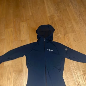 Marinblå jacka från Sail Racing - Snygg marinblå jacka från Sail Racing med huva och dragkedja. Perfekt för kyligare dagar med sin stilrena design och funktionella detaljer. Passar bra för både vardag och utomhusaktiviteter.