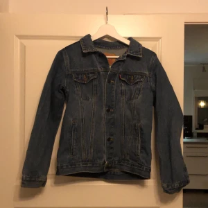 Jeansjacka från Levi Strauss & Co. - Snygg jeansjacka från Levi Strauss & Co. i klassisk blå denim. Jackan har långa ärmar och knappar framtill samt två bröstfickor med lock. Perfekt för en avslappnad stil. Knappt andvänd.