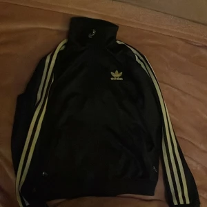 svart och guldig adidas hoodie - svart och guldig adidas hoodie i bra skick. använt ett par gånger men inte på länge. skriv för fler frågor!