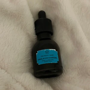 Himalayan Charcoal Night Peel från The Body Shop - En flaska med Himalayan Charcoal Skin Clarifying Night Peel från The Body Shop. Produkten kommer i en mörk glasflaska med pipett för enkel applicering. Perfekt för att förnya och klarna huden under natten.