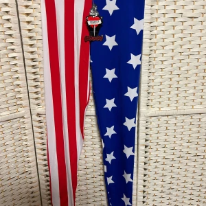 Färgglada leggings med stjärnor och ränder - Snygga leggings med ett unikt mönster av röda och vita ränder på ena benet och blått med vita stjärnor på det andra. Perfekta för att sticka ut och visa din personliga stil. Tillverkade i ett stretchigt material för en bekväm passform.